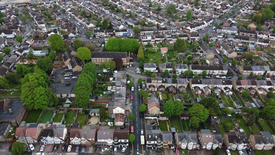 An aerial view of a residential neighbourhood showing tightly packed terraced houses with pitched roofs, some of which have patches of snow. The street runs centrally through the image, lined with par